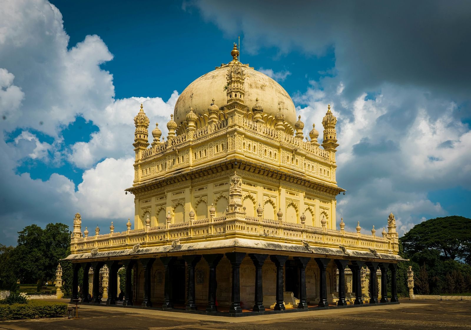 Exterior photograph of a temple with a large dome and pillars, against a cloudy sky.