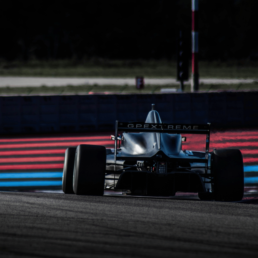 A back view of a formula 4 car driving along in the Formula 1 Qatar with red and blue streaks in front of the car.