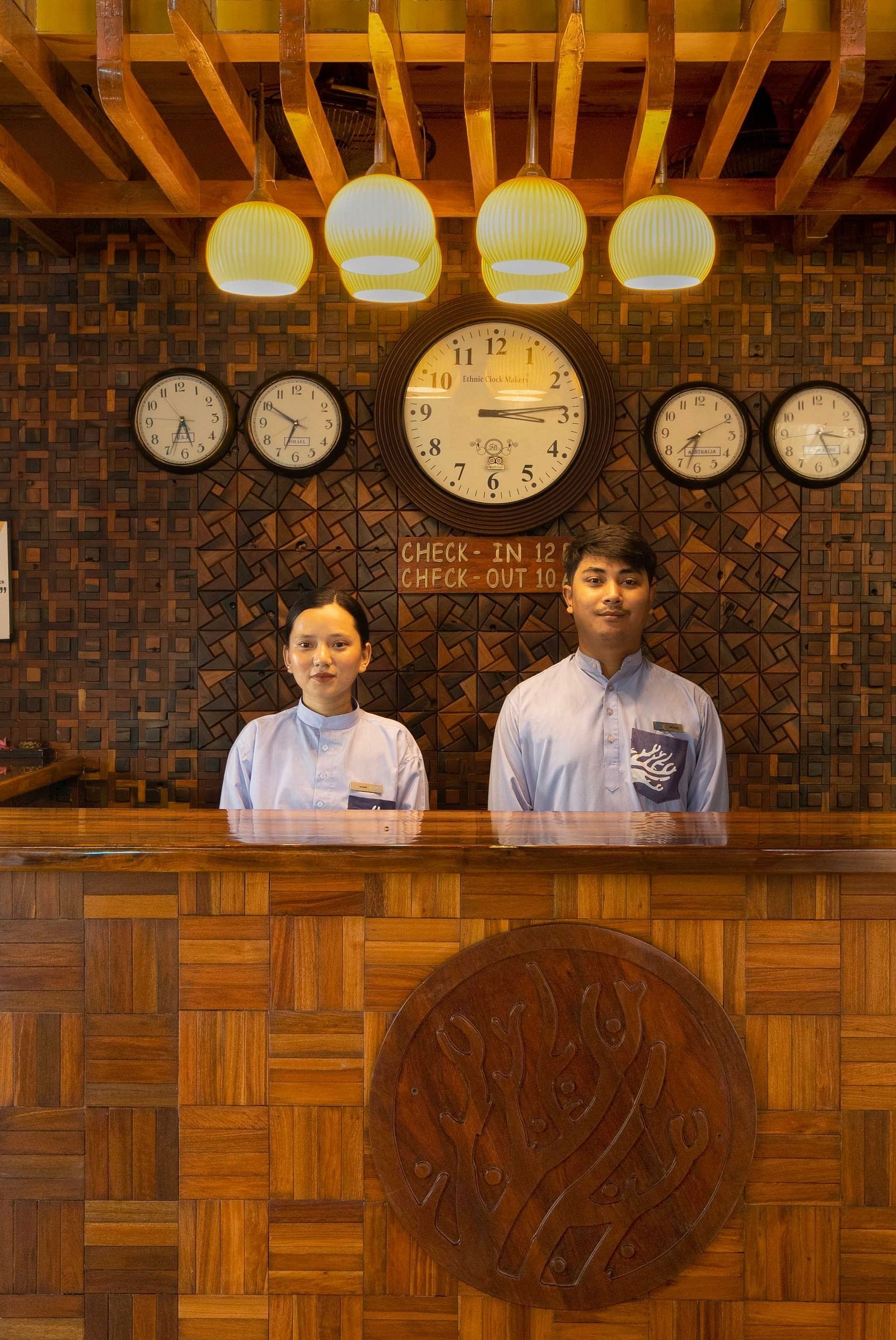 A reception area with two friendly staff members behind a wooden desk, decorated with plants and soft lighting. The space is welcoming and stylish with natural materials - Coral Reef Resort & Spa, Havelock
