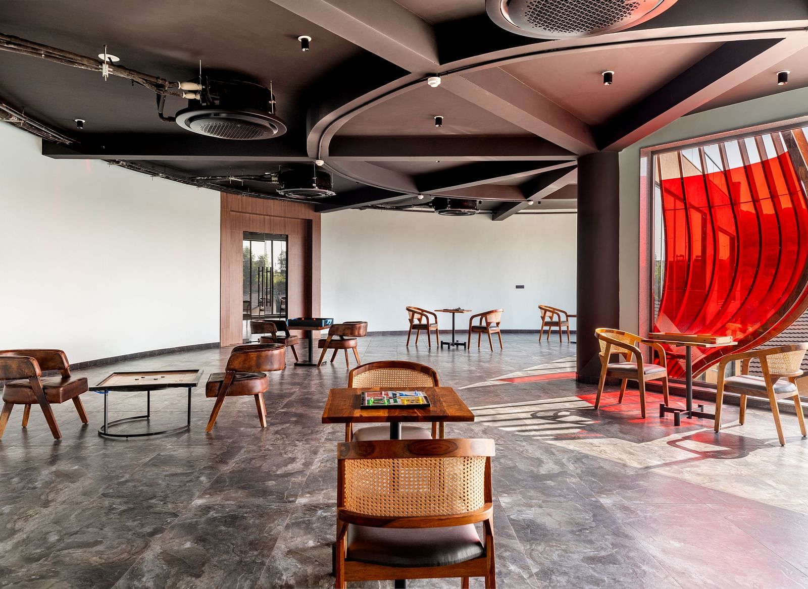 An indoor games area at The Qualia Resort Club & Brewery, Udaipur featuring unique seating arrangements, a dark ceiling with track lighting, and a partial view of a red curtain.
