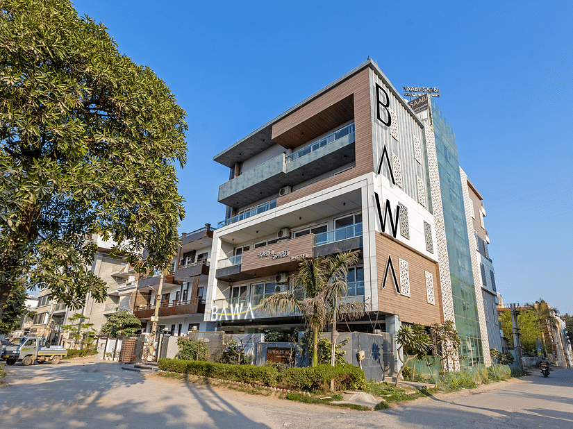 Exterior view of  the facade of Hotel Bawa, Gurgaon, a multi-storeyed building with a tree in the foreground and a clear blue sky in the background.