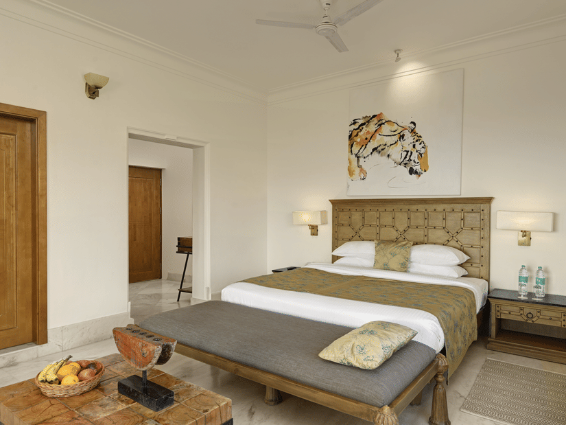 Bedroom of Valley View Suite with Jacuzzi at Fateh Safari Suites, Kumbhalgarh featuring double size bed, bedside table with electric lamps on either side, a sofa in front of the bed and then a centre table with fruits.