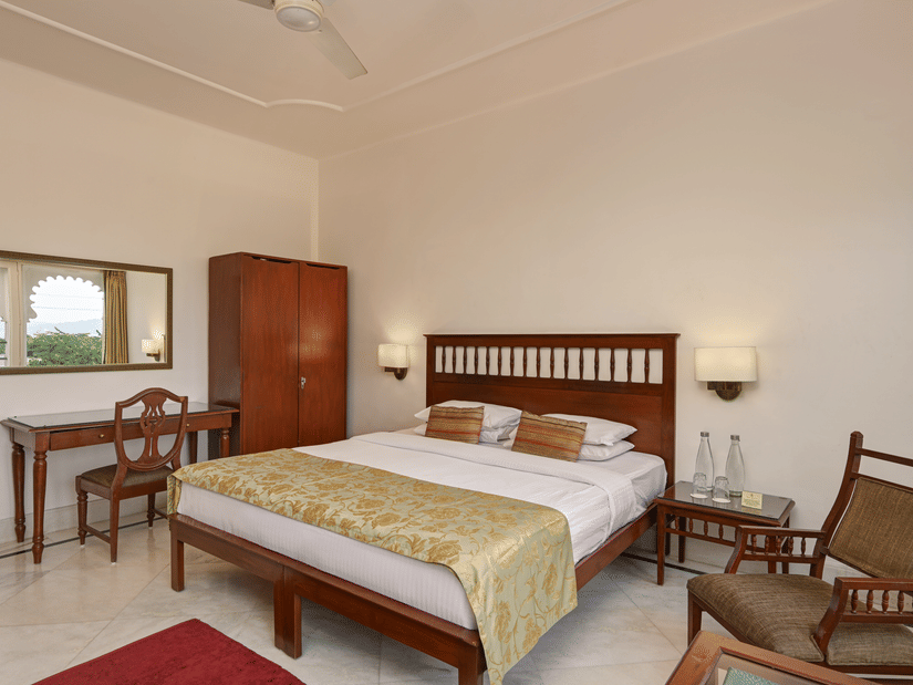 Elegant room with king bed, wooden furniture, flat-screen TV, and warm ambiance at Ram Pratap Palace, Udaipur.