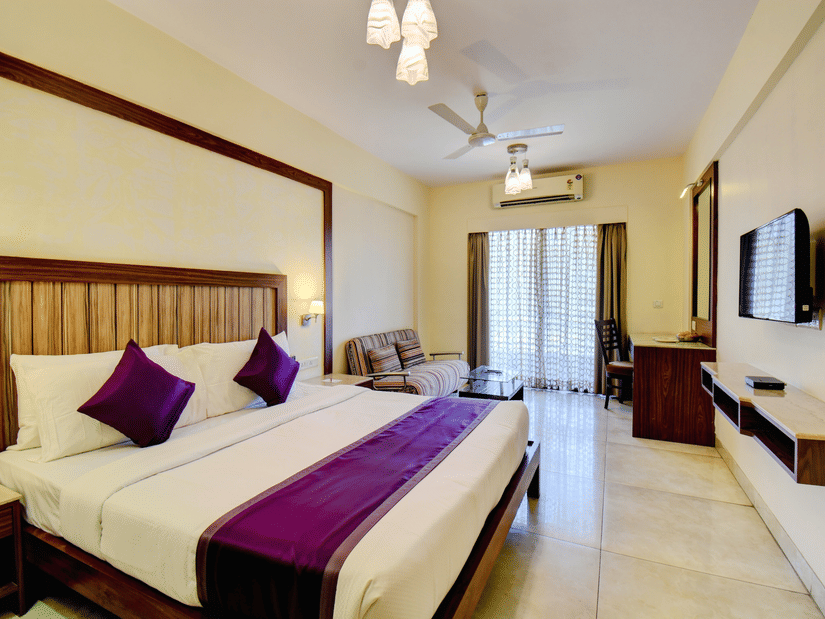 Deluxe King Room with a king size bed, seating area, and balcony door at VITS Lonavala.
