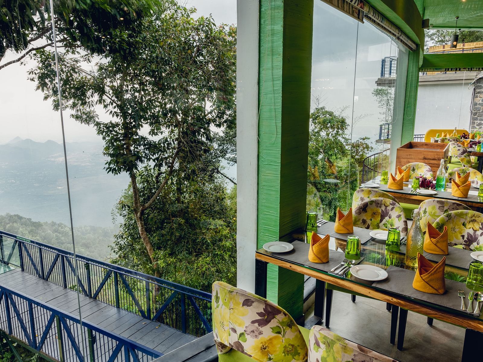 An image of a restaurant with seating arrangement and expansive glass window over looking the serene mountains - Great Trails Yercaud by GRT Hotels