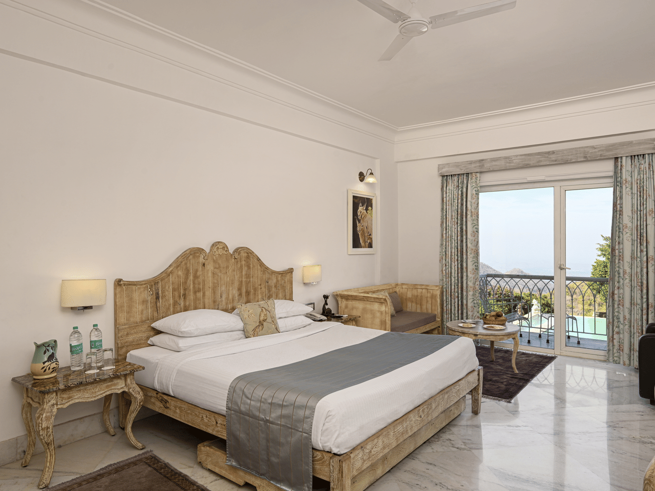 Superior Room with Balcony at Fateh Safari Resort, Kumbhalgarh featuring a double size bed, a bedside table with water bottles, a sofa with centre table, and a balcony with plunge pool with a view of the hill.
