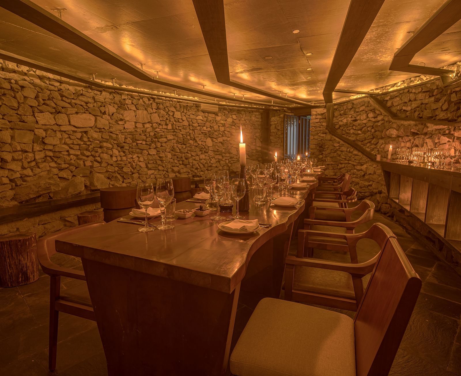 Long wooden dining table with chairs and a candlelit setting.
