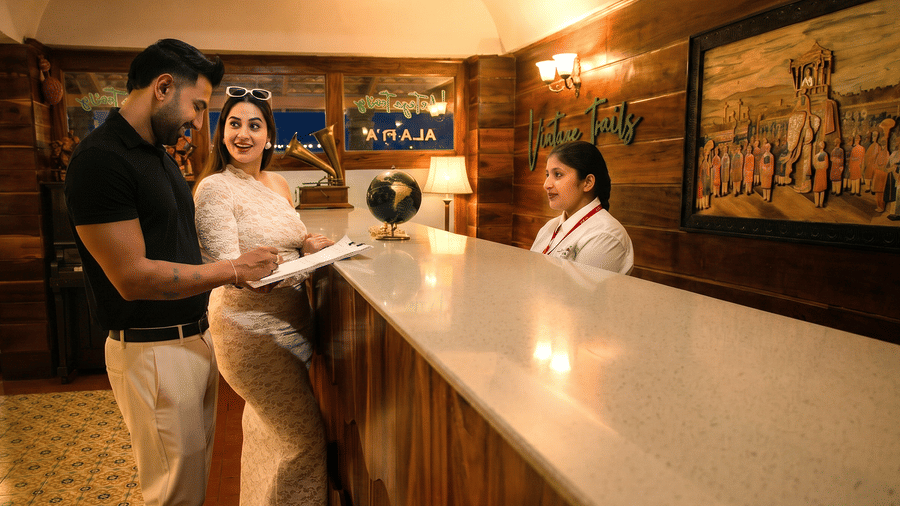 A man and a woman speaking to a receptionist standing behind a long, glossy white reception counter | Vintage Trails By Ilara