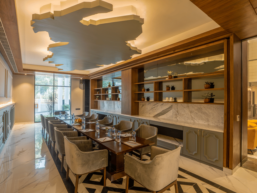 Private dining room with long table, grey upholstered chairs, sculpted ceiling and marble floor at Polo Hotel, Agartala.