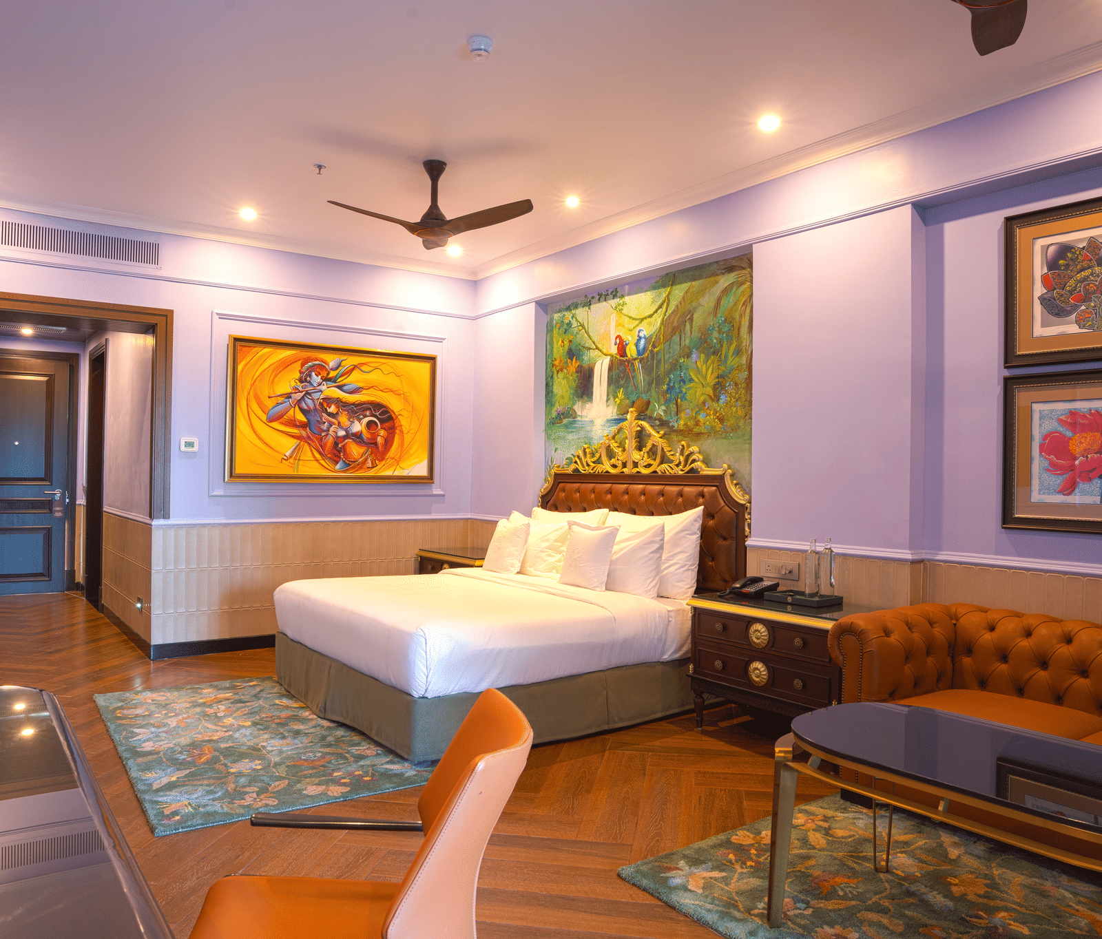 A room with a king size bed, seating area, and vibrant, large abstract paintings decorating the wall space at MAYFAIR Bay Resort, Paradeep.