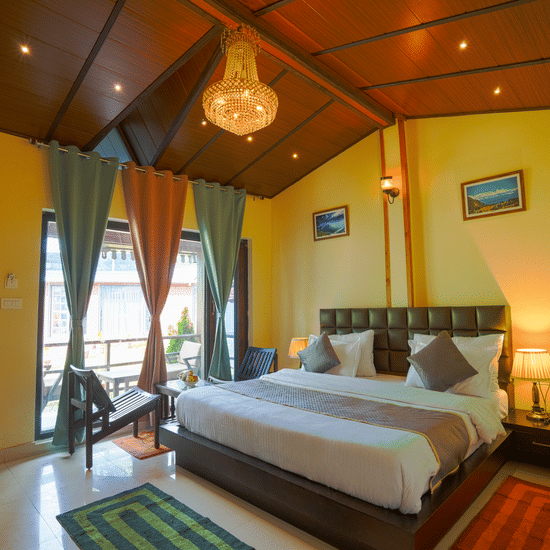 A bedroom featuring a neatly made bed with cushions, bedside lamps, 2 chairs and a coffee table, and a chandelier | Sol Glow Resort, Nainital