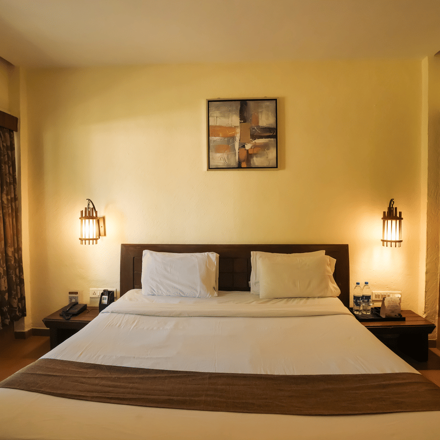 A warm, cozy resort room featuring a double bed flanked by glowing bedside lamps next to a large window.