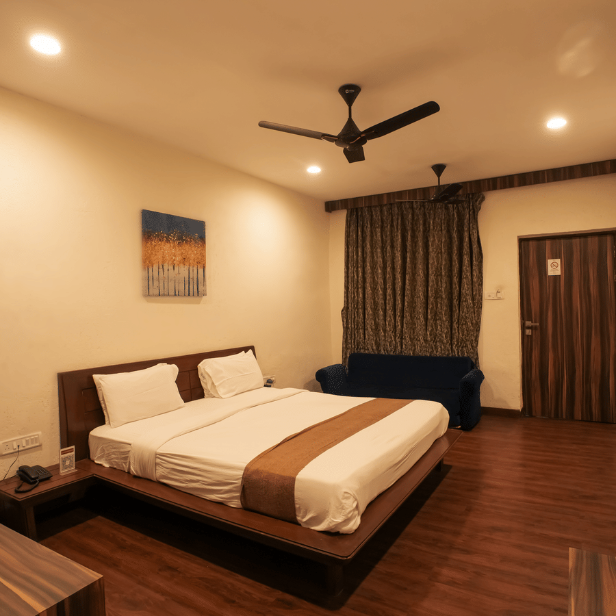 A resort bedroom layout featuring a double bed, dark wood furniture accents, a blue couch, and a wall-mounted TV.