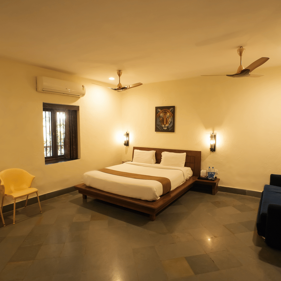 A large hotel room featuring a double bed, a dark blue sofa, and two vibrant yellow accent chairs.
