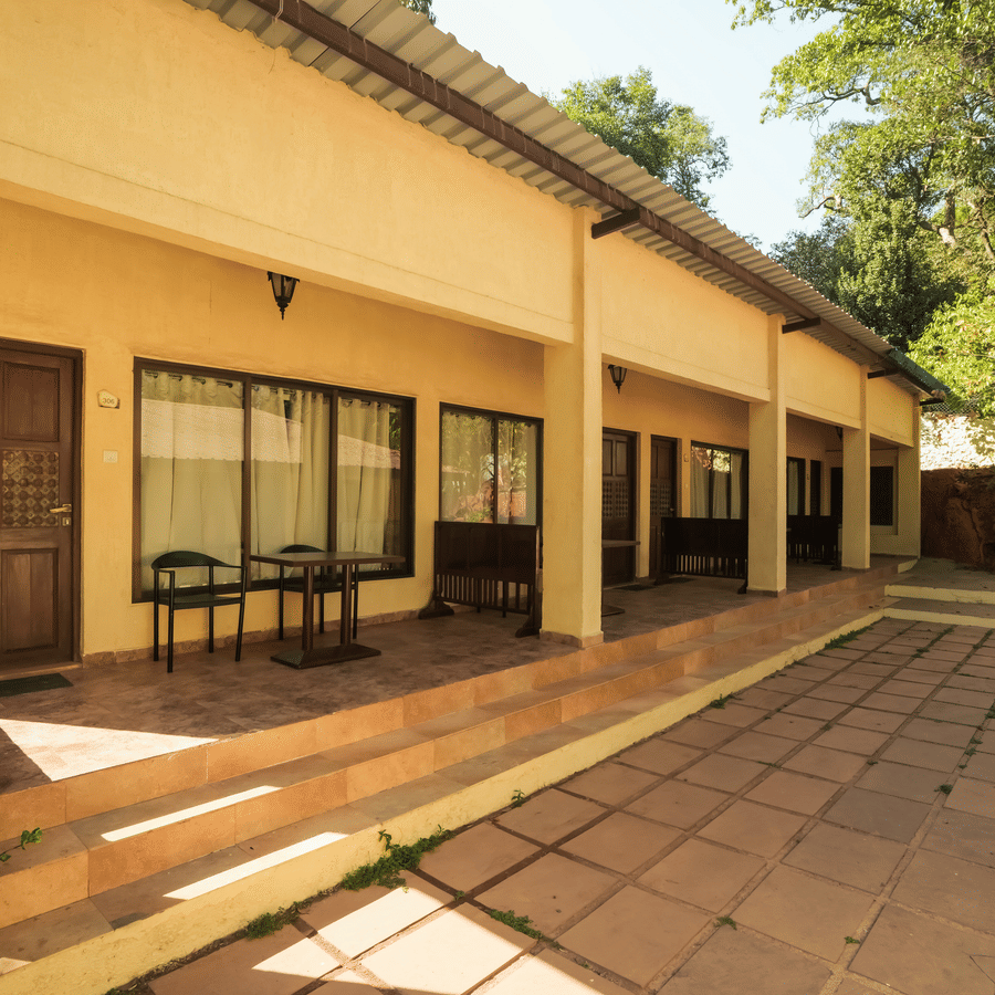 A daytime exterior view of a cream-colored resort villa block with a wide, open stone-paved courtyard.
