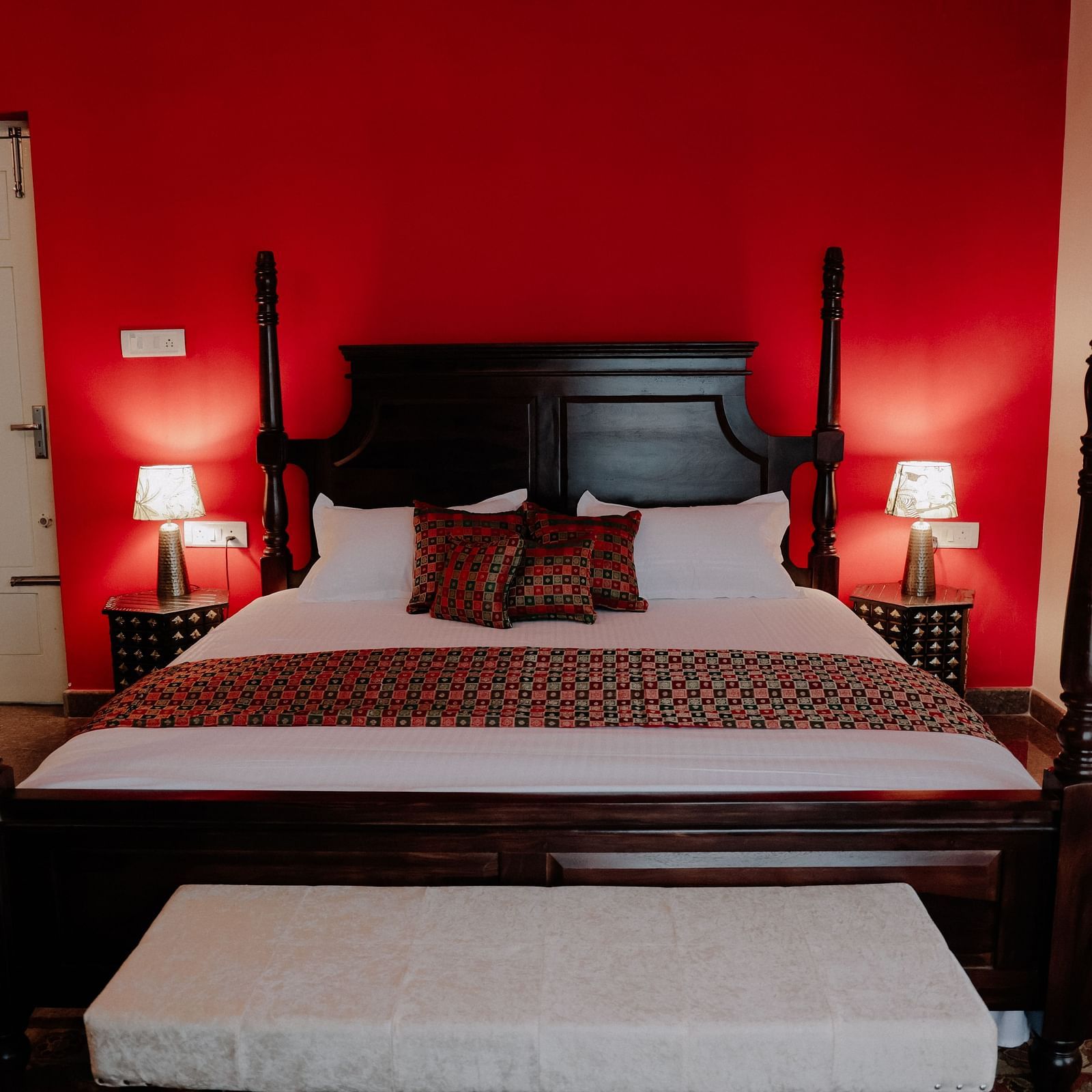 A dark wood four-poster bed with white linens and a patterned throw in a room with a bold red wall | Adhyaya Heritage Reverbed