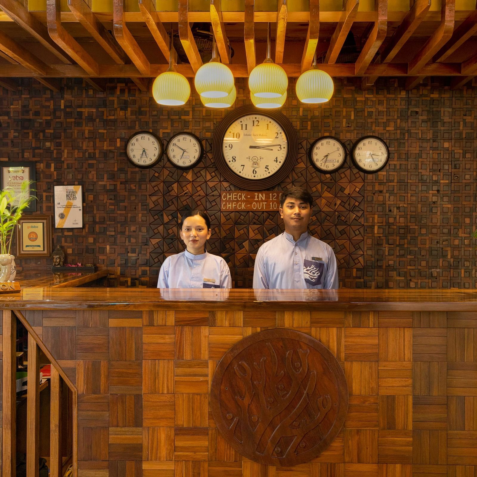 A reception area with two friendly staff members behind a wooden desk, decorated with plants and soft lighting. The space is welcoming and stylish with natural materials - Coral Reef Resort & Spa, Havelock