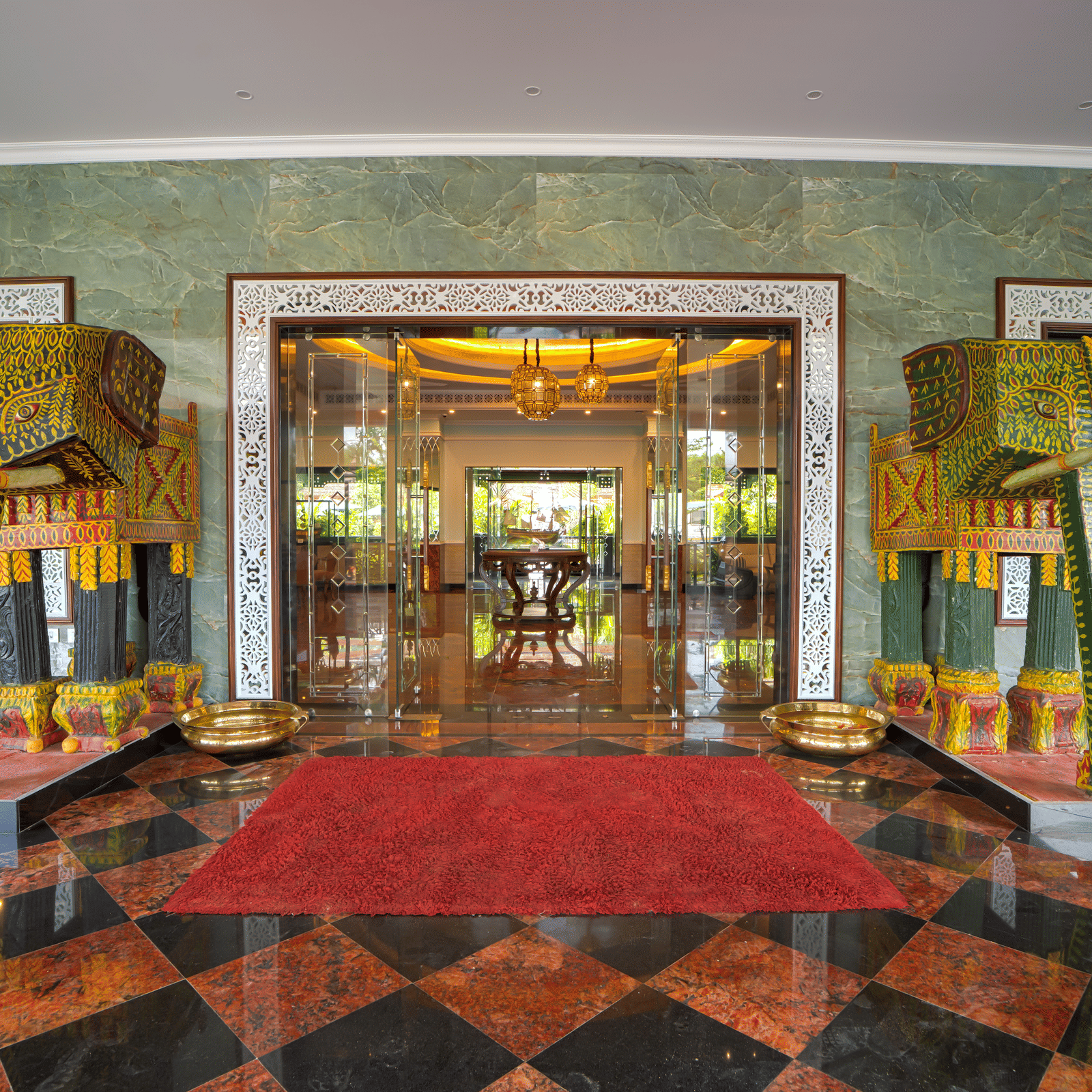 A grand entrance lobby with polished flooring, red carpet, ornate pillars, large glass doors and symmetrical décor including golden accents at MAYFAIR Bay Resort, Paradeep.