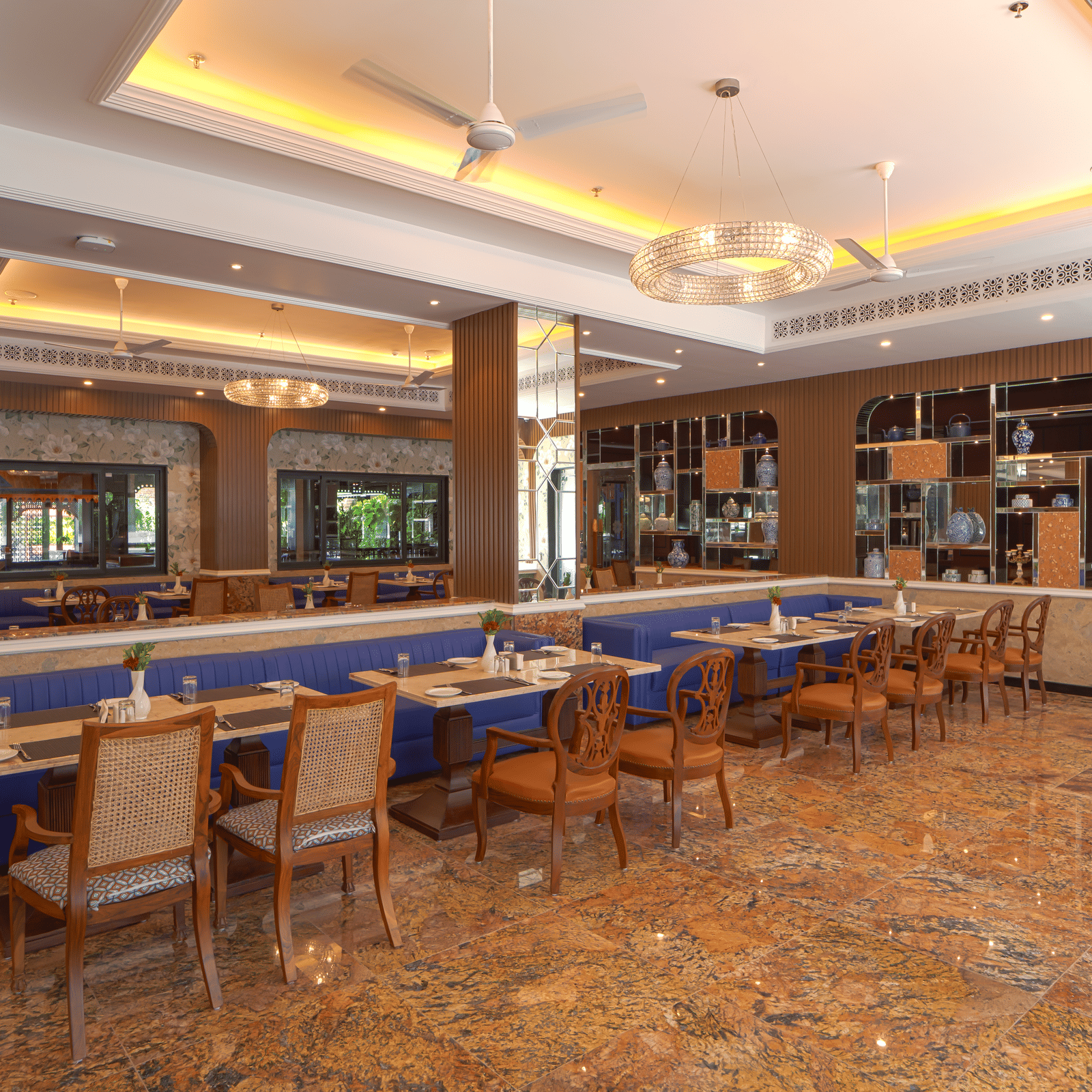 A restaurant hall with wooden chairs, dining tables, recessed ceiling lights and wide windows providing natural light at MAYFAIR Bay Resort, Paradeep.