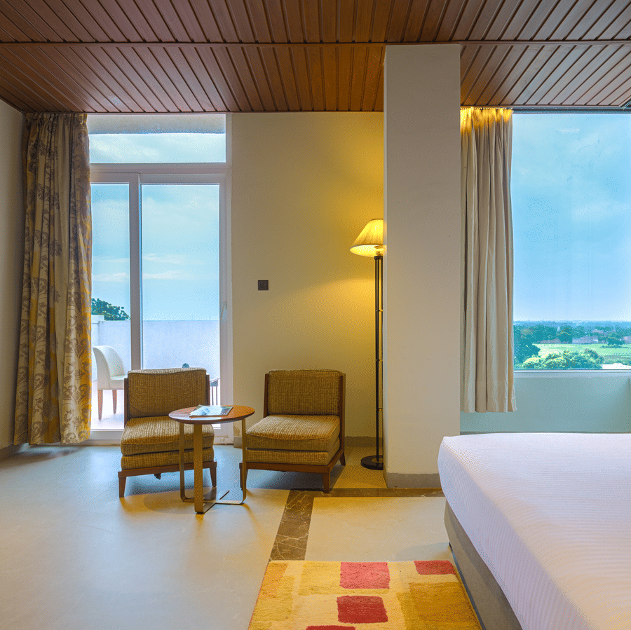 Hotel bedroom with a king size bed, armchair, large windows, curtains and views of the surrounding landscape.