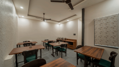 Side view of a dining room with dark wooden tables, chairs, and ceiling fans - Perfectstayz Value Aalaya Suites, Haridwar