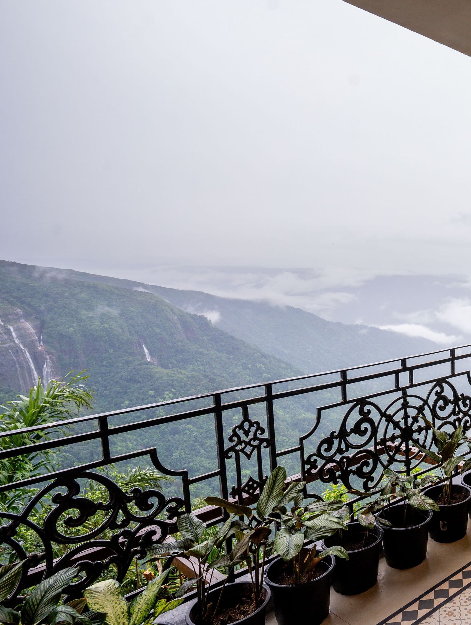 A balcony seating with potted plants overlooking the misty Seven Sisters Waterfalls - Polo Resort Cherrapunjee