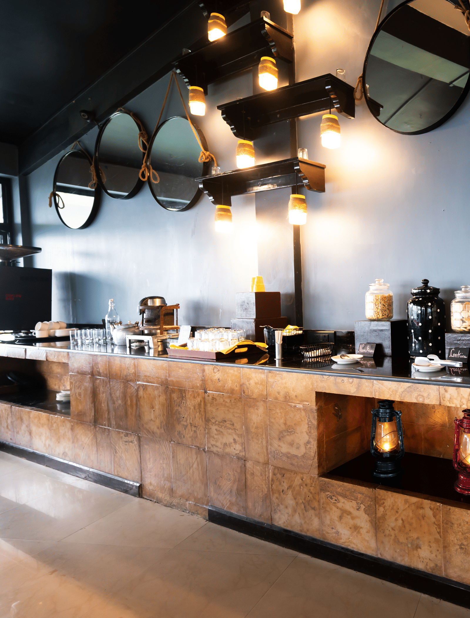 Bar counter at Polo Resort Cherrapunji with circular hanging mirrors, colourful lanterns underneath and snack jars on a wooden-tiled counter.