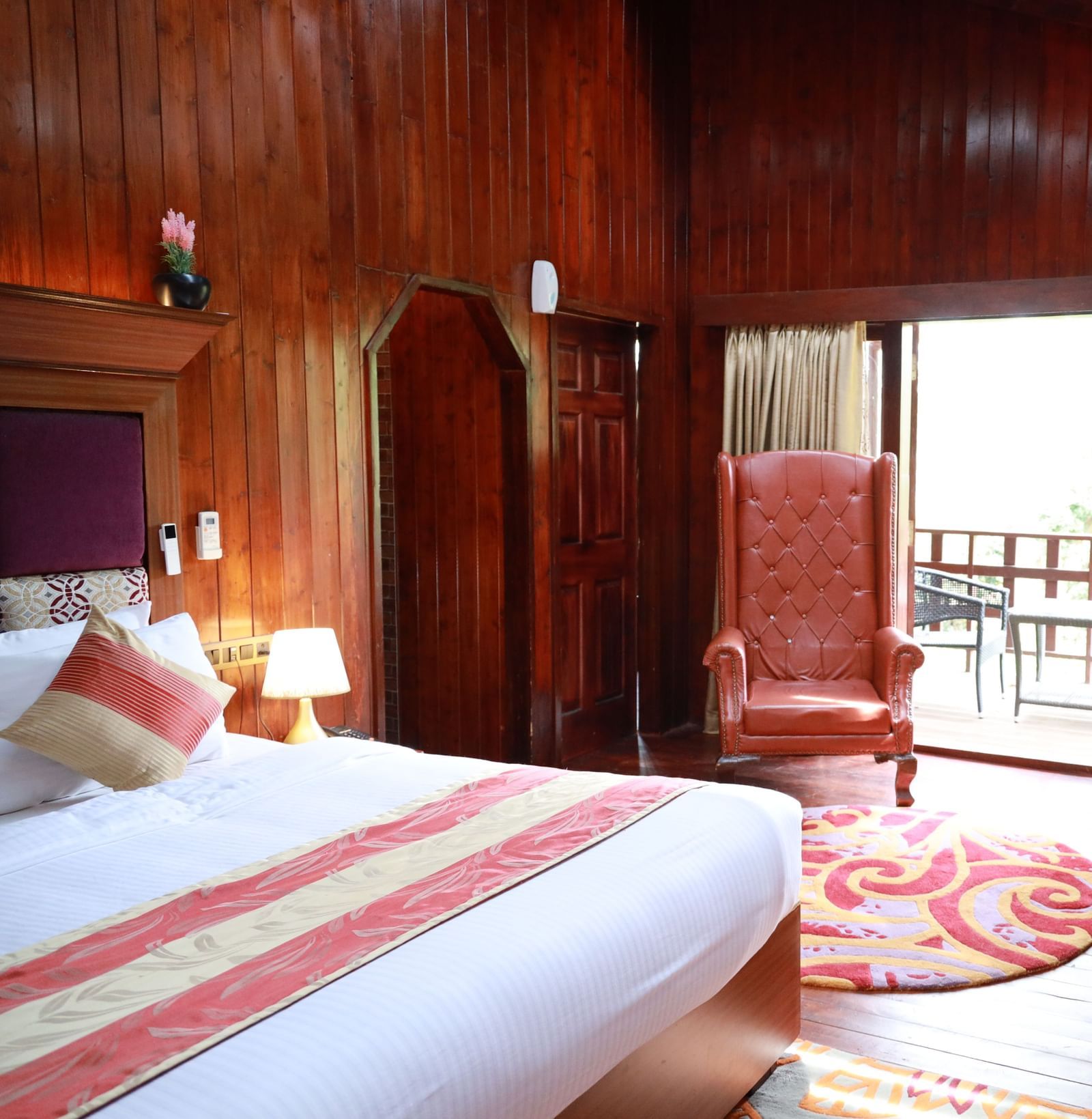 A wide angle shot of a hotel room in Ooty featuring a king bed, a wall-mounted television and a balcony with stunning views - Accord Highland Ooty
