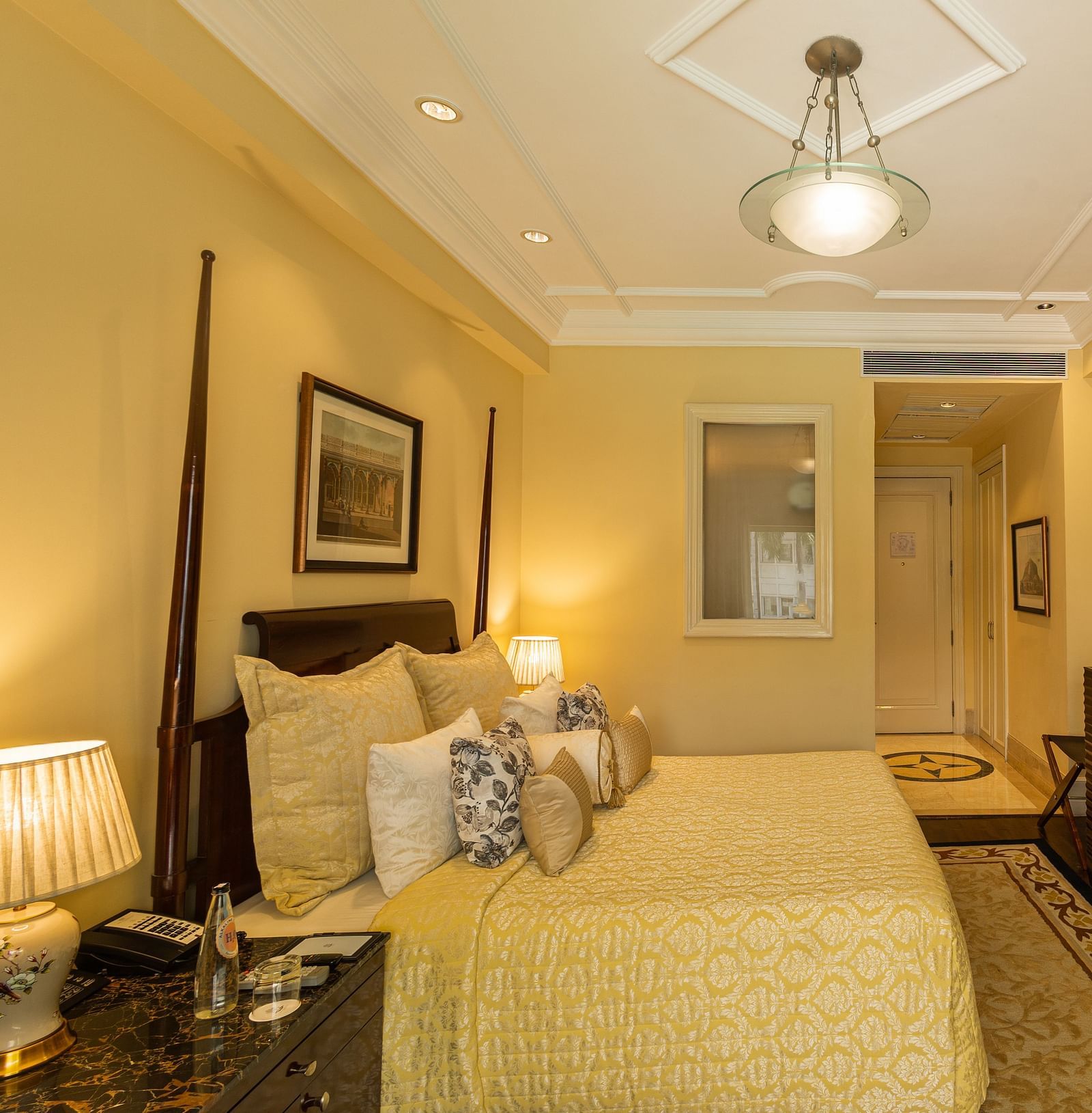 Side view of the Deluxe King Bed Room Pool View at The Claridges New Delhi, featuring a cosy king sized bed, wall-mounted TV, and bedside lamps