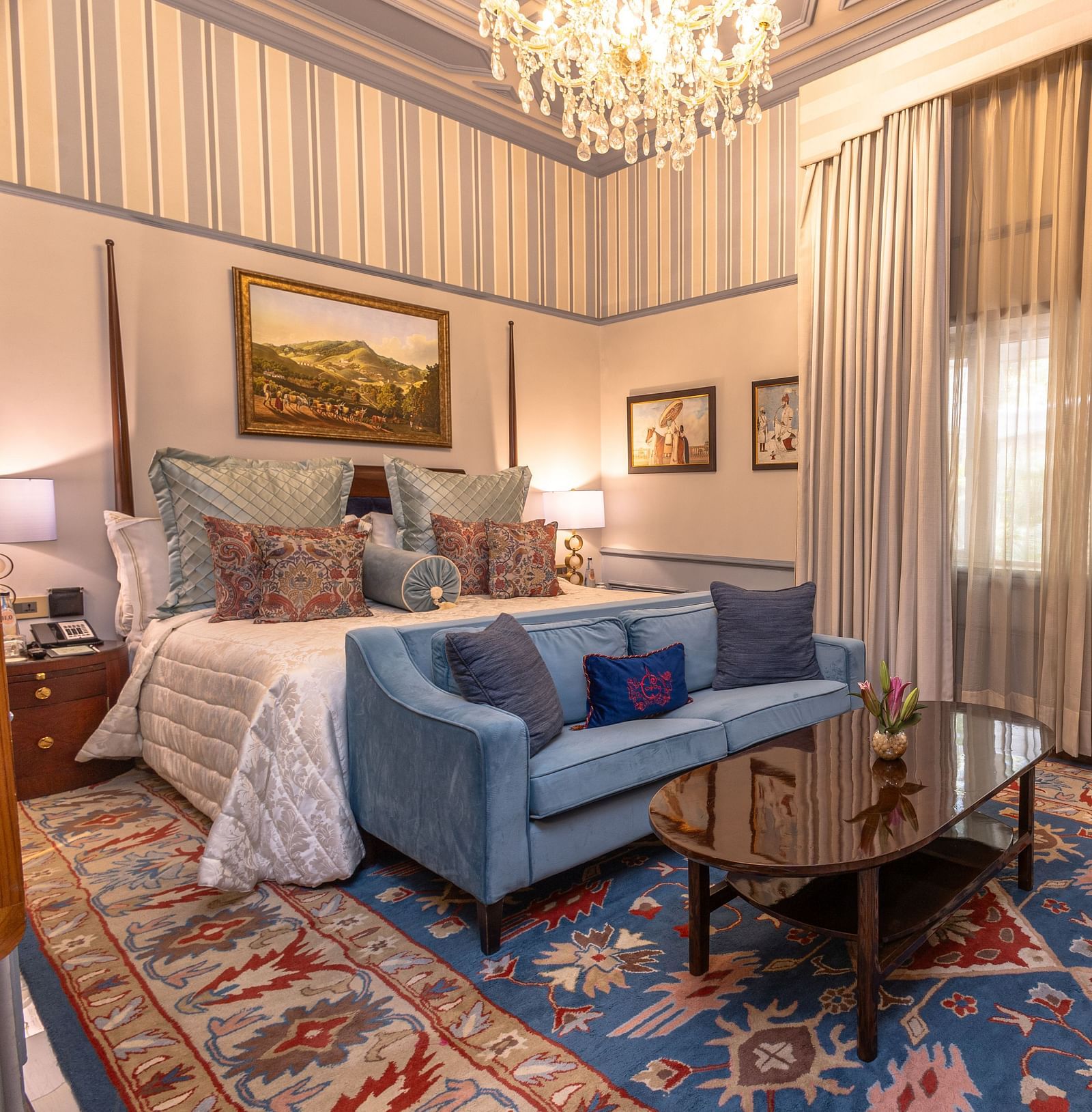 image of the brightly lit bedroom with a king size bed and blue couch place in front of the bed at our heritage parlour suites - The Claridges New Delhi