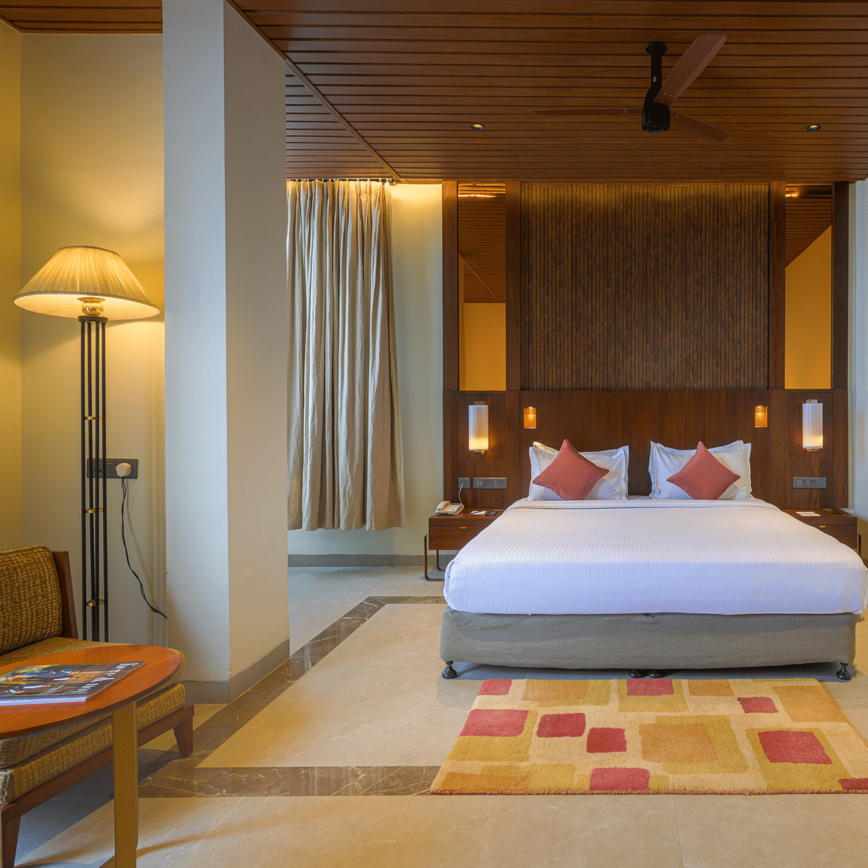 Hotel bedroom with a king size bed, patterned rug, wooden ceiling, bedside tables and warm ambient lighting.