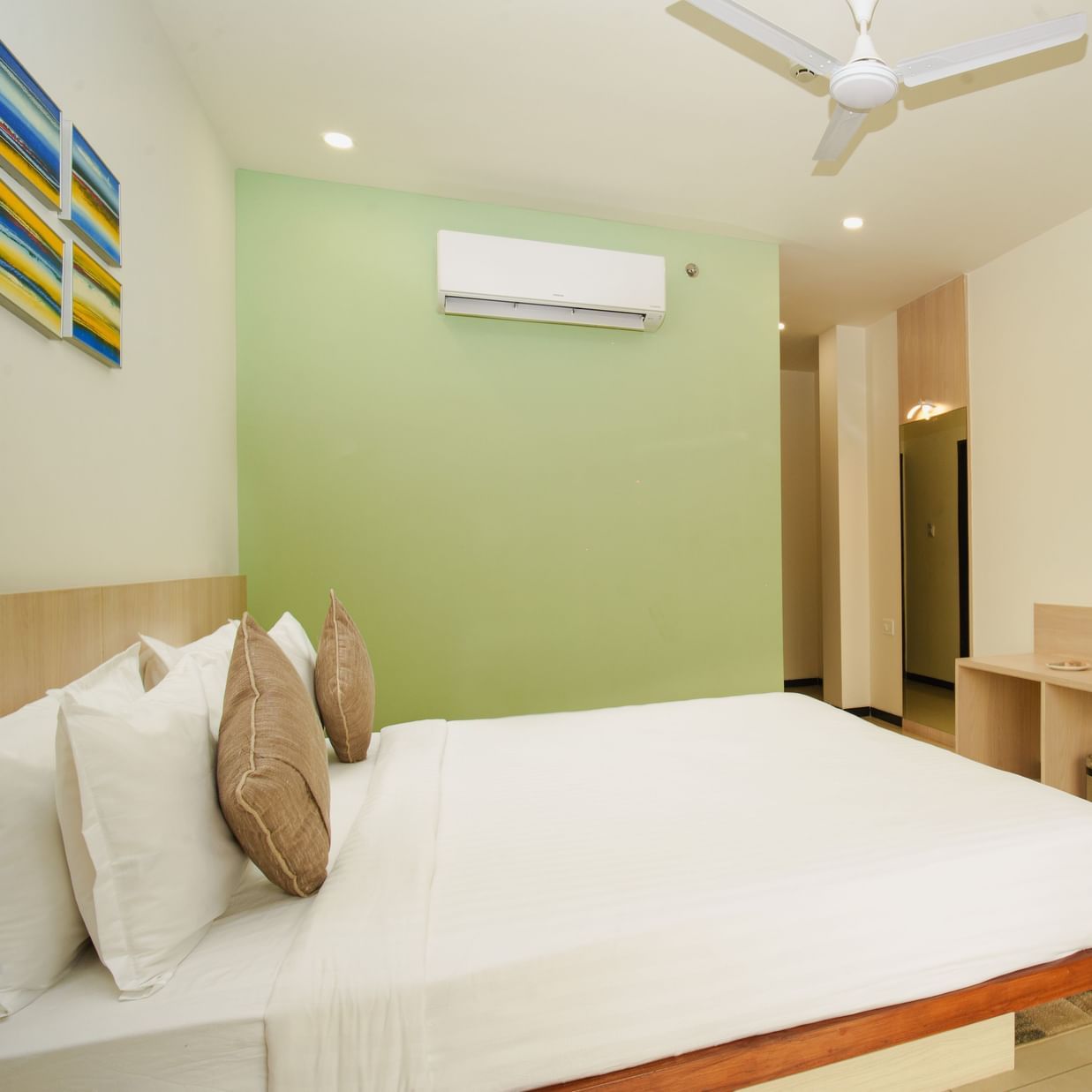Hotel room with a large bed, desk, wall-mounted television, and a subtle green accent wall at Arawali Ananta Elite, Jaipur.
