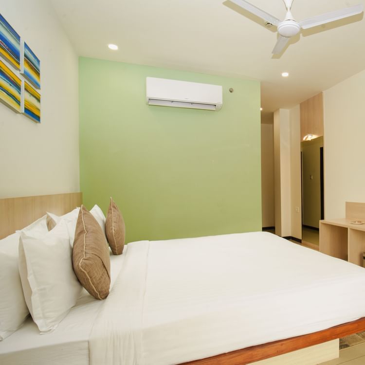 Hotel room with a large bed, desk, wall-mounted television, and a subtle green accent wall at Arawali Ananta Elite, Jaipur.