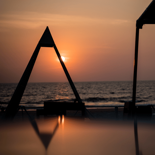 unset over the ocean with silhouetted beach structures and reflections on wet sand.