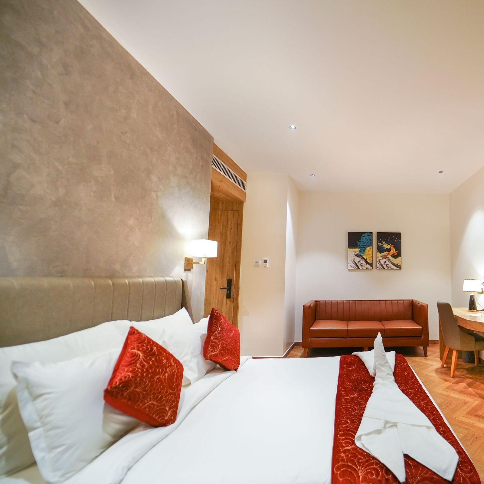 A spacious hotel room features a bed with decorative linens, pillows, a sofa, a desk area, and a mounted television - Hotel Park Inn, Nellore.