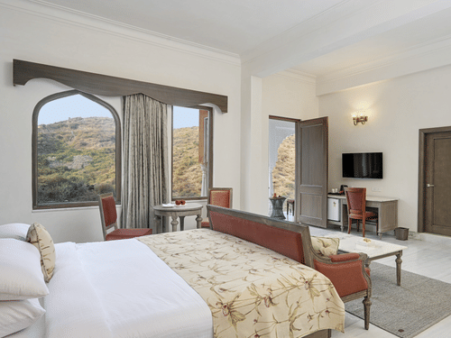 Fateh Vilas Udaipur - interior view of the suite featuring a king size bed a work desk a television and windows with curtains