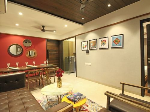 A living and dining area with furniture, red accent wall, wall art, and warm ambient lighting.