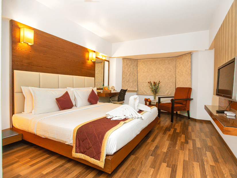 Spacious executive room with a king sized bed, wooden flooring, warm lighting, and modern amenities at Monarch Luxur Hotel, Bangalore.