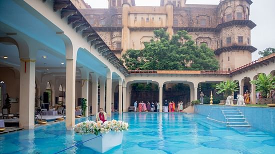 A swimming pool with blue patterned tiles is surrounded by covered walkways and the historic architecture of Tijara Fort-Palace - 19th Century, Alwar.