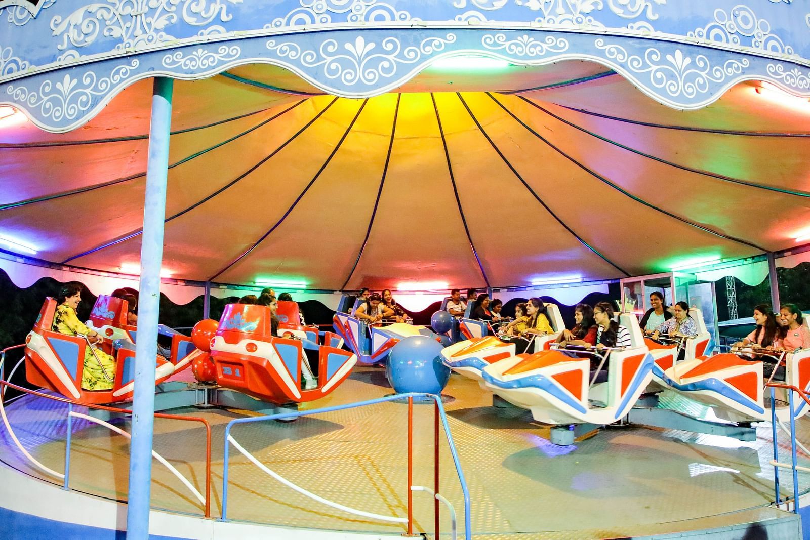 Visitors enjoy a colorful Break Dance ride under a canopy at Ramoji Film City, with vibrant lights enhancing the atmosphere.