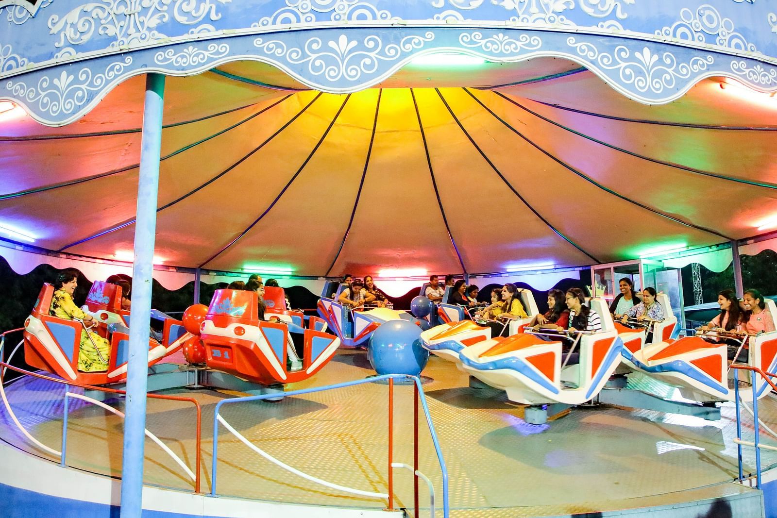 Visitors enjoy a colorful Break Dance ride under a canopy at Ramoji Film City, with vibrant lights enhancing the atmosphere.
