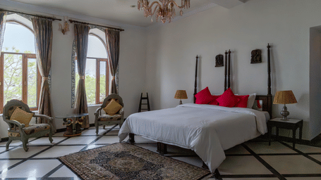 A spacious bedroom at Fort Barli, Ajmer, features a four-poster bed, seating area, and large windows.