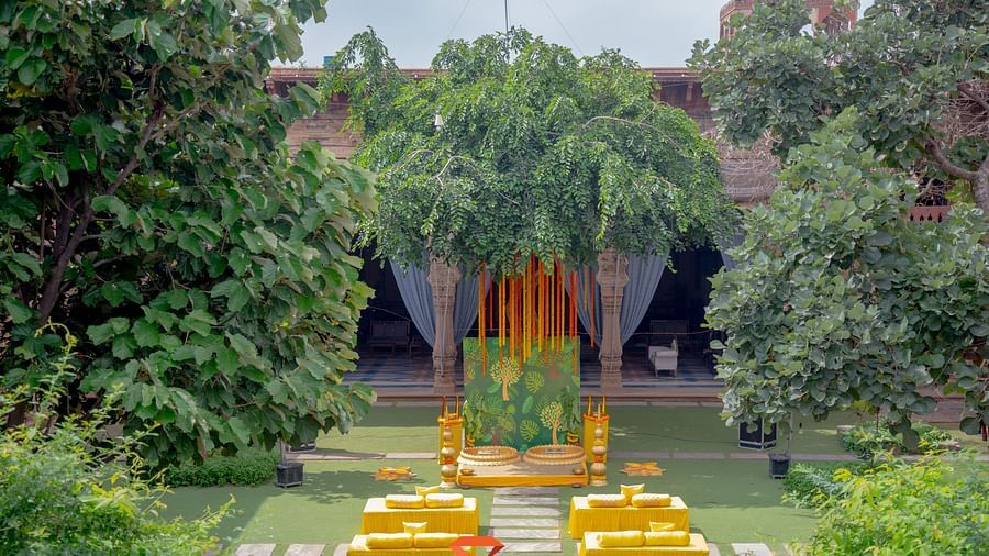 An outdoor event setup with yellow seating and a decorated stage is nestled among the trees at Tijara Fort-Palace - 19th Century, Alwar.