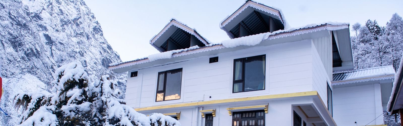 facade view of Mystique Valley Resort covered with snow, surrounded by pine trees, parked bikes, and cars, offering a serene winter retreat in a Himalayan setting.