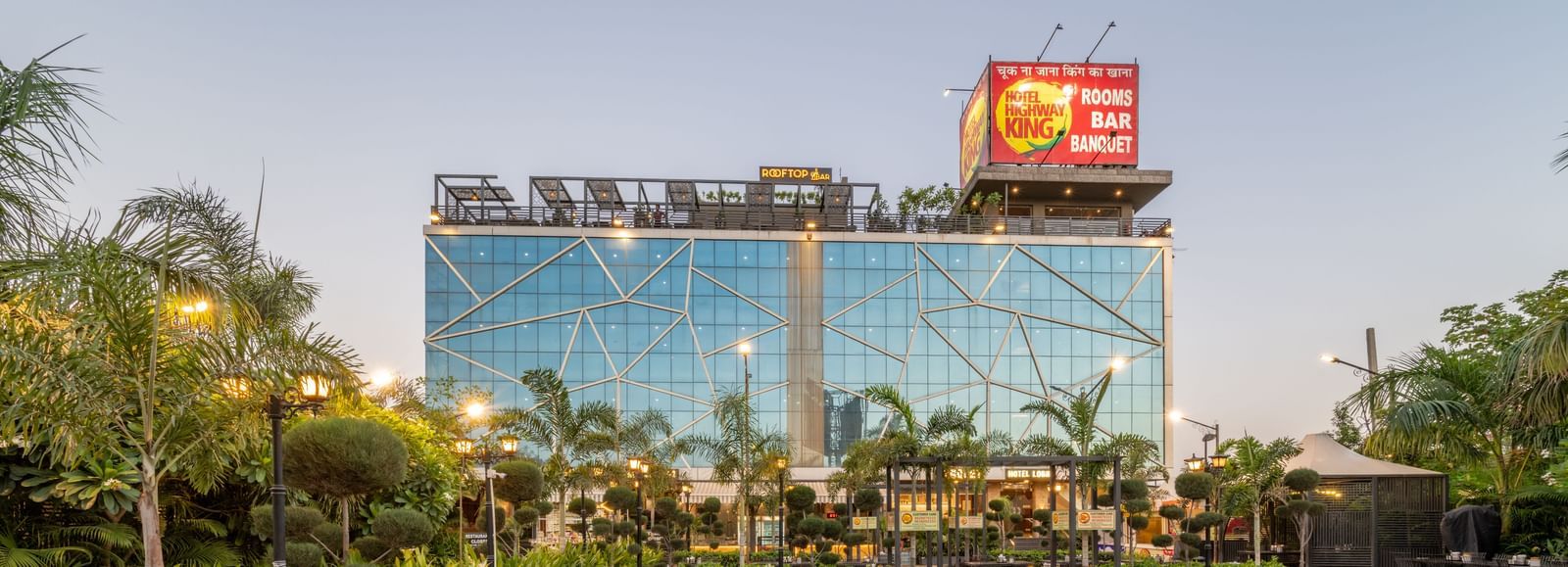 Outdoor seating area with multiple tables and chairs arranged in rows with greenery and the facade of Hotel Highway King at the background.