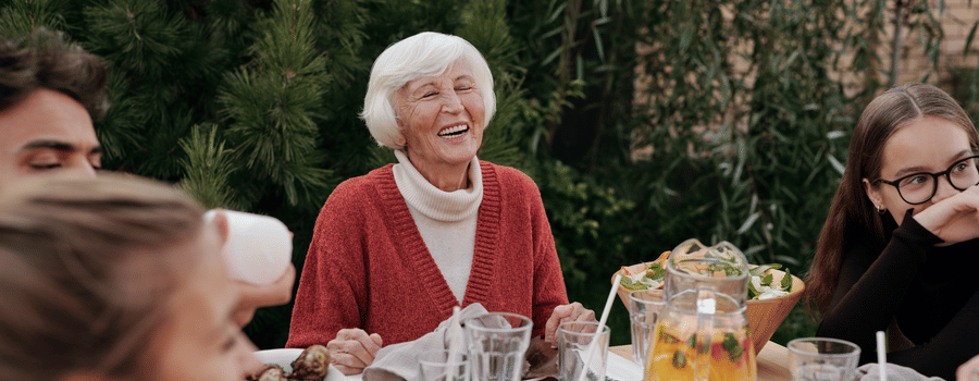 Family gathered around an outdoor dining table, sharing a joyful meal with drinks and laughter