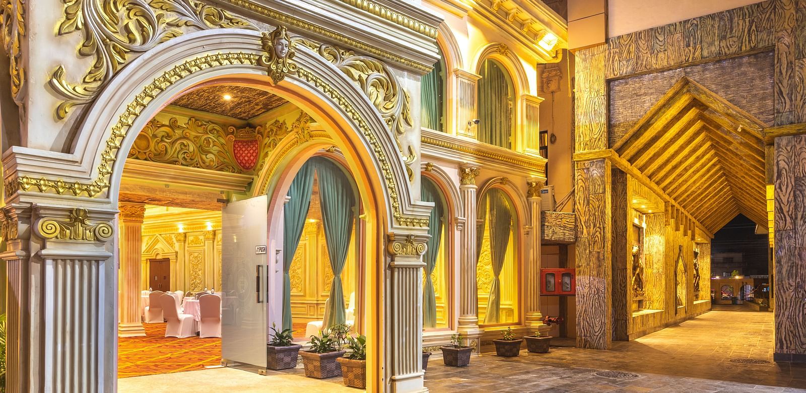 Ornately decorated entrance of Diamond Palace Lords Plaza at night with arched doorways and a reflective stone walkway.