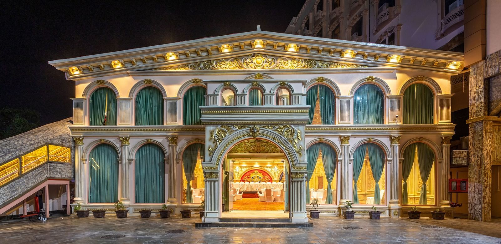 Illuminated facade of Diamond Palace Lords Plaza at night with arched windows, ornate details, and a wet stone courtyard.