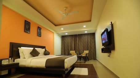 A spacious bedroom at Krushnai Resort with a bed, an orange wall, and a large TV mounted on the wall.