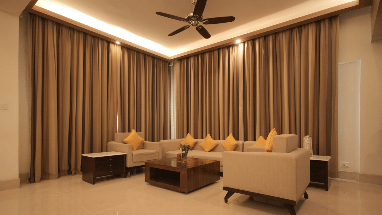 A living room with comfortable sofas, a center table, floor-to-ceiling curtains, and warm lighting in the Presidential Suite at Clarks Amer, Jaipur.